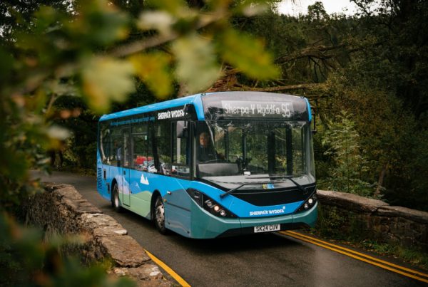 Sherpa bus crossing a bridge surrounded by leafy scenery near Snowdon, perfect for reaching hiking trails from Lodge Dinorwig